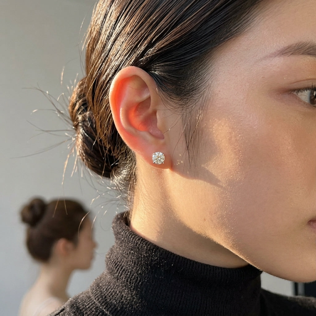 a close-up of a woman's ear wearing a small round 1 ct stud earring with a clear gemstone, set against a softly blurred background.