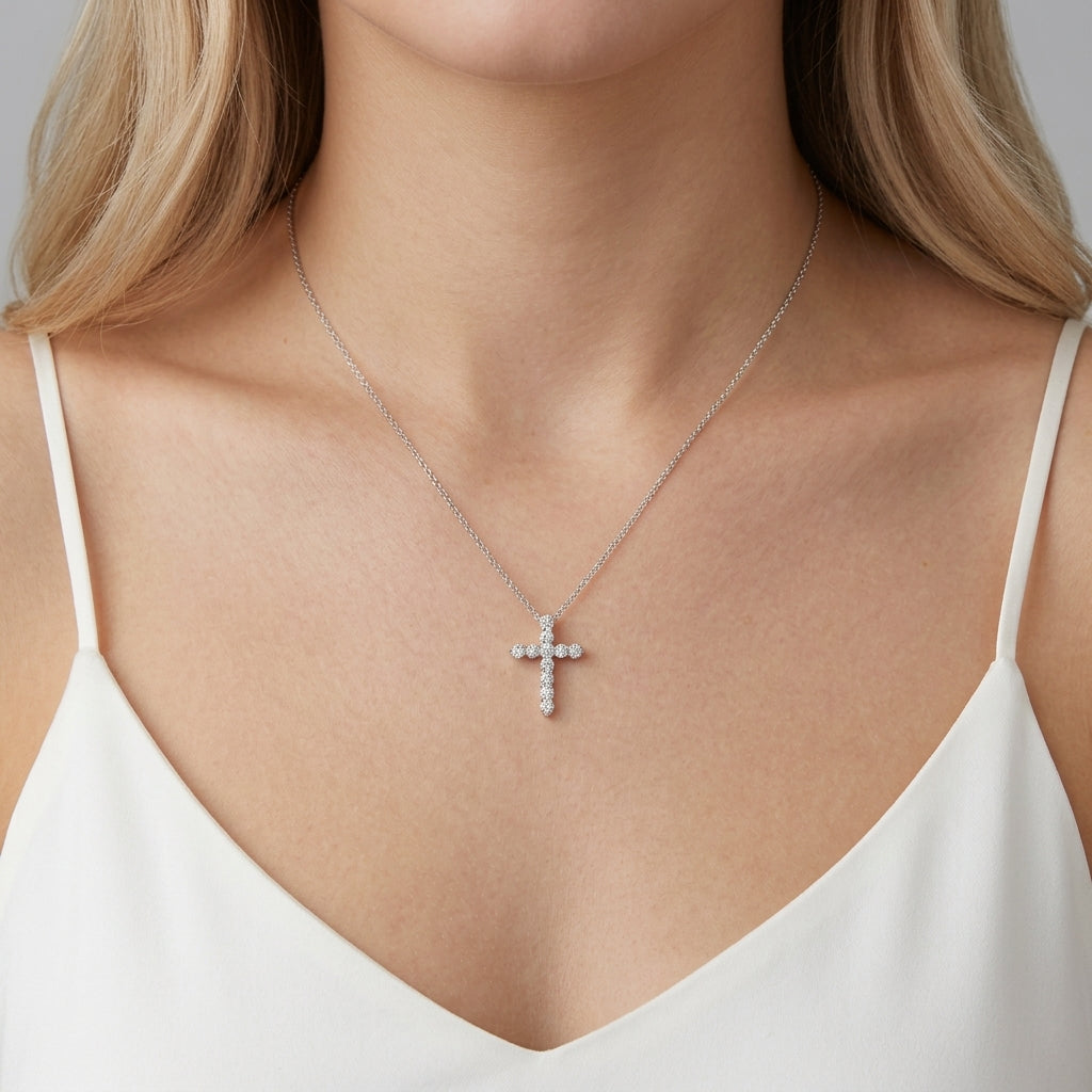 A close-up of a woman wearing a delicate 14k gold cross pendant necklace adorned with 0.1 ct diamonds, styled with a white camisole top.